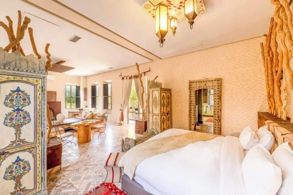 Een ruime slaapkamer met een groot bed, een bureau, een stoel, een decoratieve spiegel en een uniek wandontwerp.
