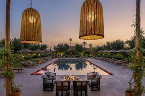 A pool area with lounge chairs, a dining table, and hanging wicker lamps. - The Source Hotel Music & Spa (Marrakech)
