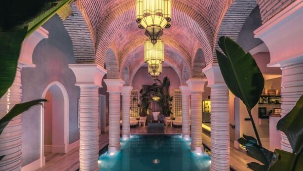 An indoor swimming pool with a central fountain, surrounded by columns and arches, and a chandelier above. - The Source Hotel Music & Spa (Marrakech)