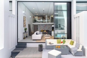 A modern interior with a sofa, coffee table, and a glass door leading to a dining area. - Elegant Pool Access Townhouse Near Beach (Koh Samui)