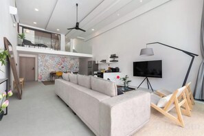 A modern living room with a sofa, a TV, and a dining area. - Elegant Pool Access Townhouse Near Beach (Koh Samui)