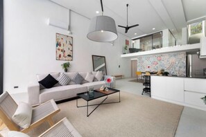 Una sala moderna con sofá, mesa de centro y comedor, con una cocina al fondo.