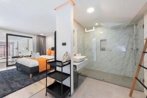 Une chambre d’hôtel moderne équipée d’un lit, d’une douche à parois de verre, d’une salle de bain avec un lavabo en marbre et d’un grand miroir.