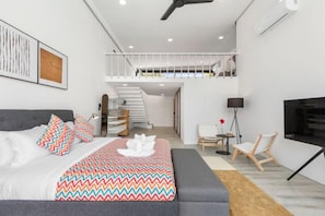 Un dormitorio moderno con cama, sofá, escalera y televisión.