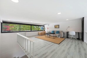 A modern living room with a sofa set, a coffee table, and a floor lamp. There is a large window providing a view of greenery outside. - Elegant Pool Access Townhouse Near Beach (Koh Samui)