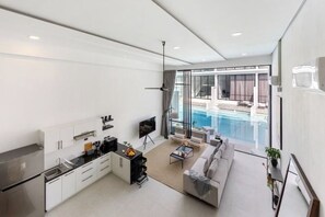 A modern living room with a kitchen, a pool view, and a large window.
