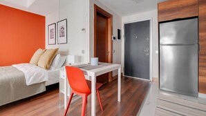 Una camera moderna con un letto, una scrivania, una sedia, un frigorifero e una porta.