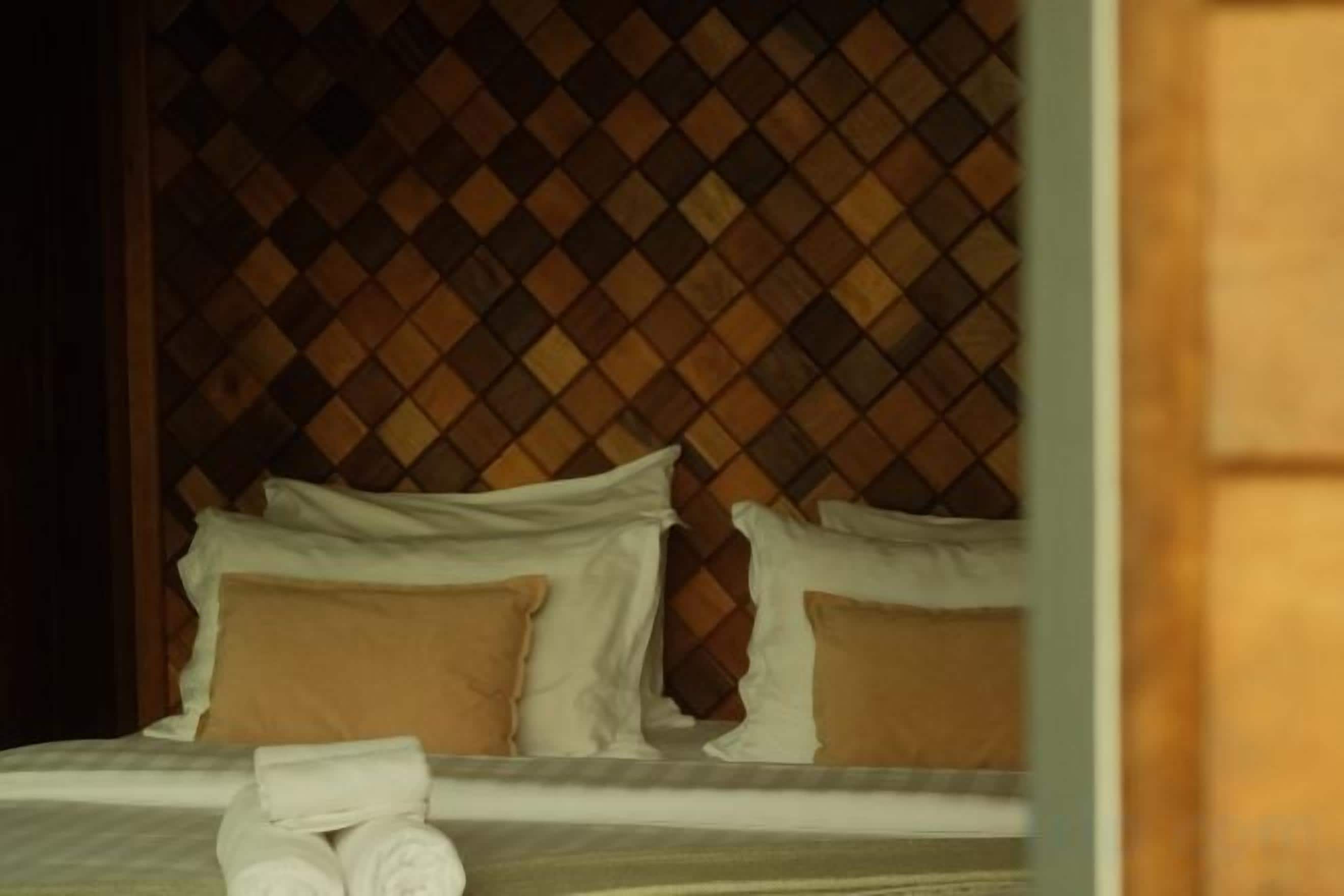Una cama con ropa blanca, almohadas marrones y una toalla doblada con cuidado sobre la cama.