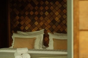 A bed with white linens and brown pillows, a wooden headboard, and a neatly folded towel on the bed.