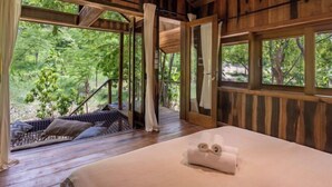 A wooden cabin with a bed, a hammock, and large windows overlooking a forest. - Payana Kampot (Makprang)