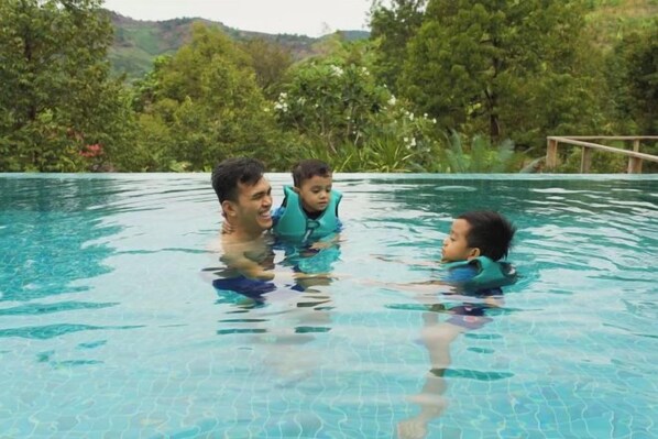 A swimming pool with clear blue water, surrounded by lush greenery and hills in the background.