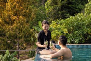 Two people sitting by a pool with greenery in the background.