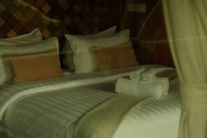 A bed with pillows and a blanket, a headboard with a diamond pattern, and a curtain partially drawn. - Payana Kampot (Makprang)