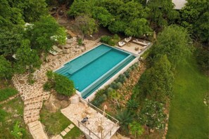 An aerial view of a rectangular swimming pool surrounded by stone walls and lush greenery. - Payana Kampot (Makprang)