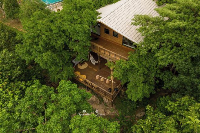 Uma cabana de madeira rodeada por uma floresta densa, com varanda e área de estar ao ar livre.