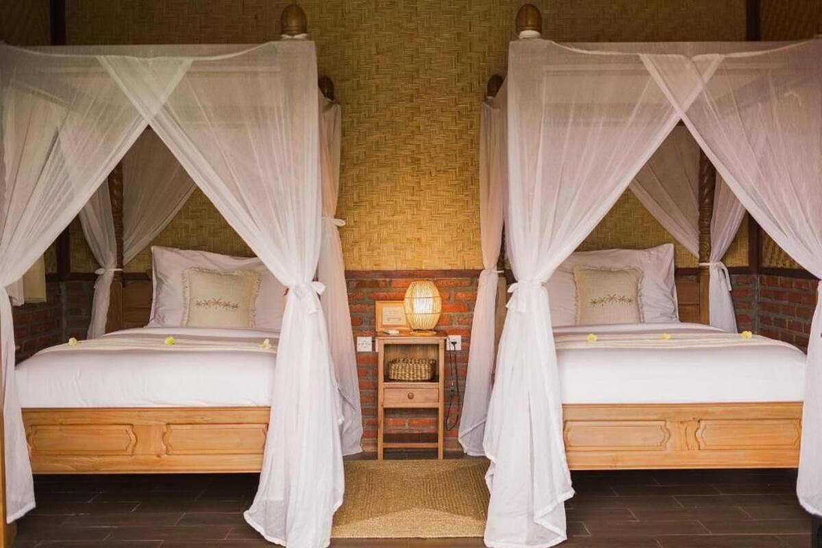 A room with two beds, each with a canopy, a small table with a lamp, and a brick wall.
