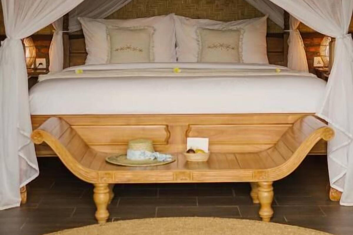 A bed with a canopy, a wooden bench, and a woven rug.