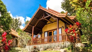 Una casa tradicional con techo de tejas, balcón de madera y un jardín con plantas tropicales.