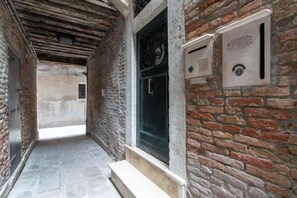 A narrow corridor with a stone floor, a door with a glass panel, and a brick wall with ventilation grilles. - Rooftop Terrace Penthouse & 360° Views Venice5th (Venice)