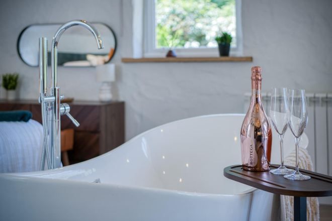 A modern bathroom with a freestanding bathtub, a mirror, and a bottle of champagne on a tray.