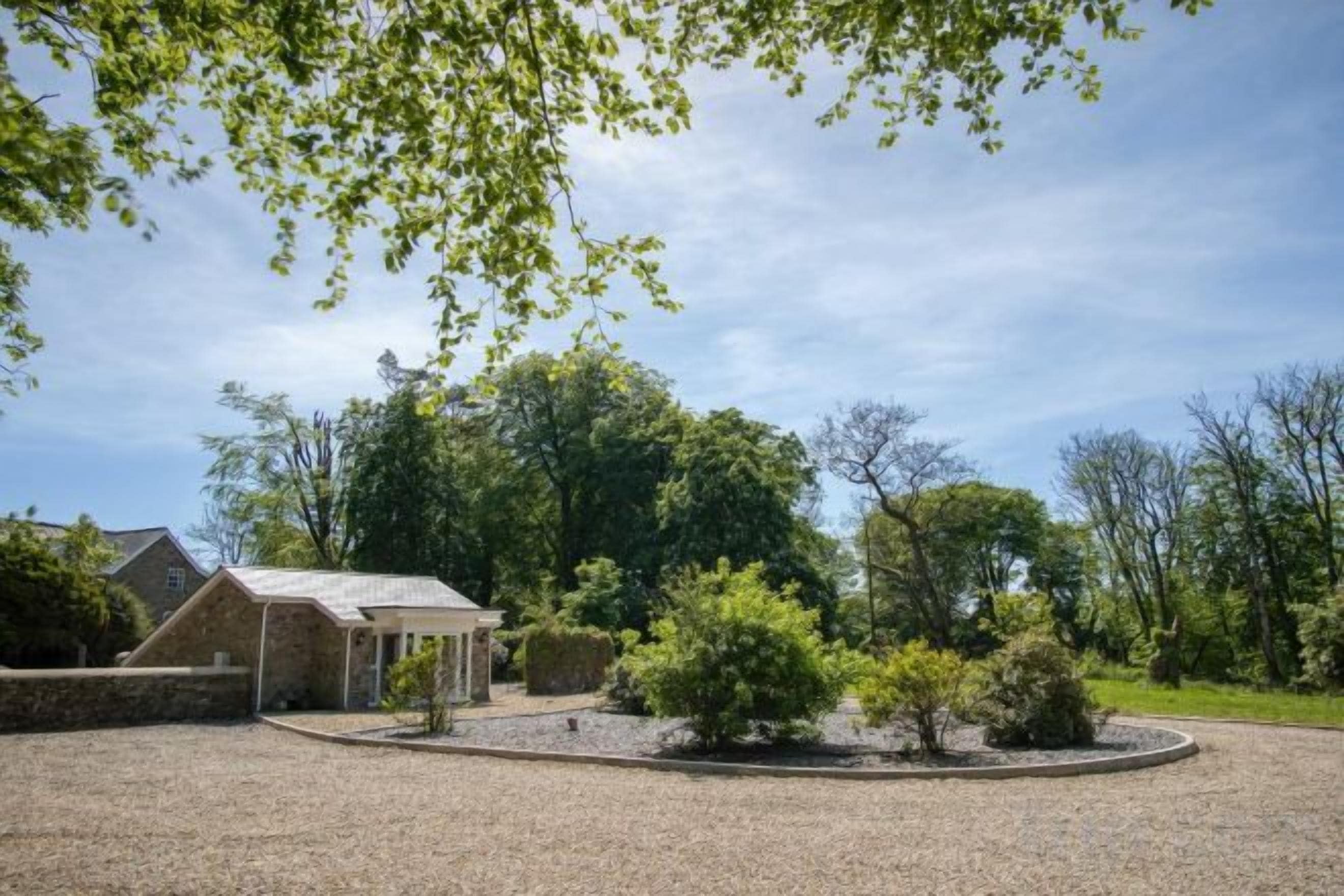 A building with a gravel driveway, surrounded by trees and a clear sky.