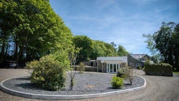 A building with a gravel driveway, surrounded by trees and shrubs.