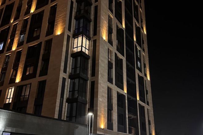 A multi-story building with illuminated windows and a prominent light fixture on the facade.