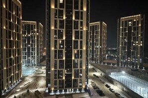 A high-rise building with multiple floors, illuminated windows, and a parking area. - Comfort City (Almaty)