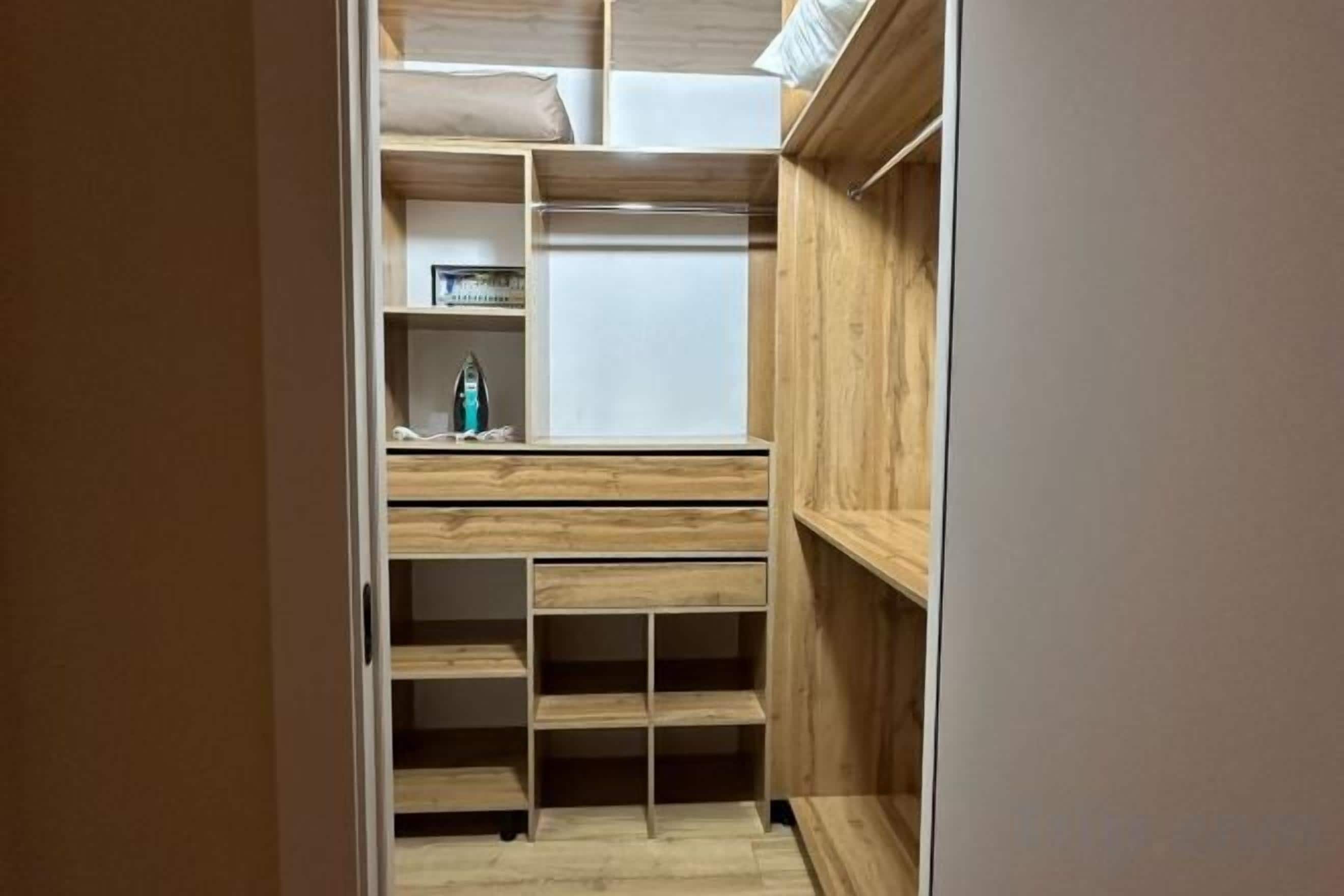 A walk-in closet with wooden shelving and drawers, a mirror, and a small shelf with a bottle.