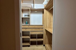 A walk-in closet with wooden shelving and drawers, a mirror, and a small shelf with a bottle. - Comfort City (Almaty)