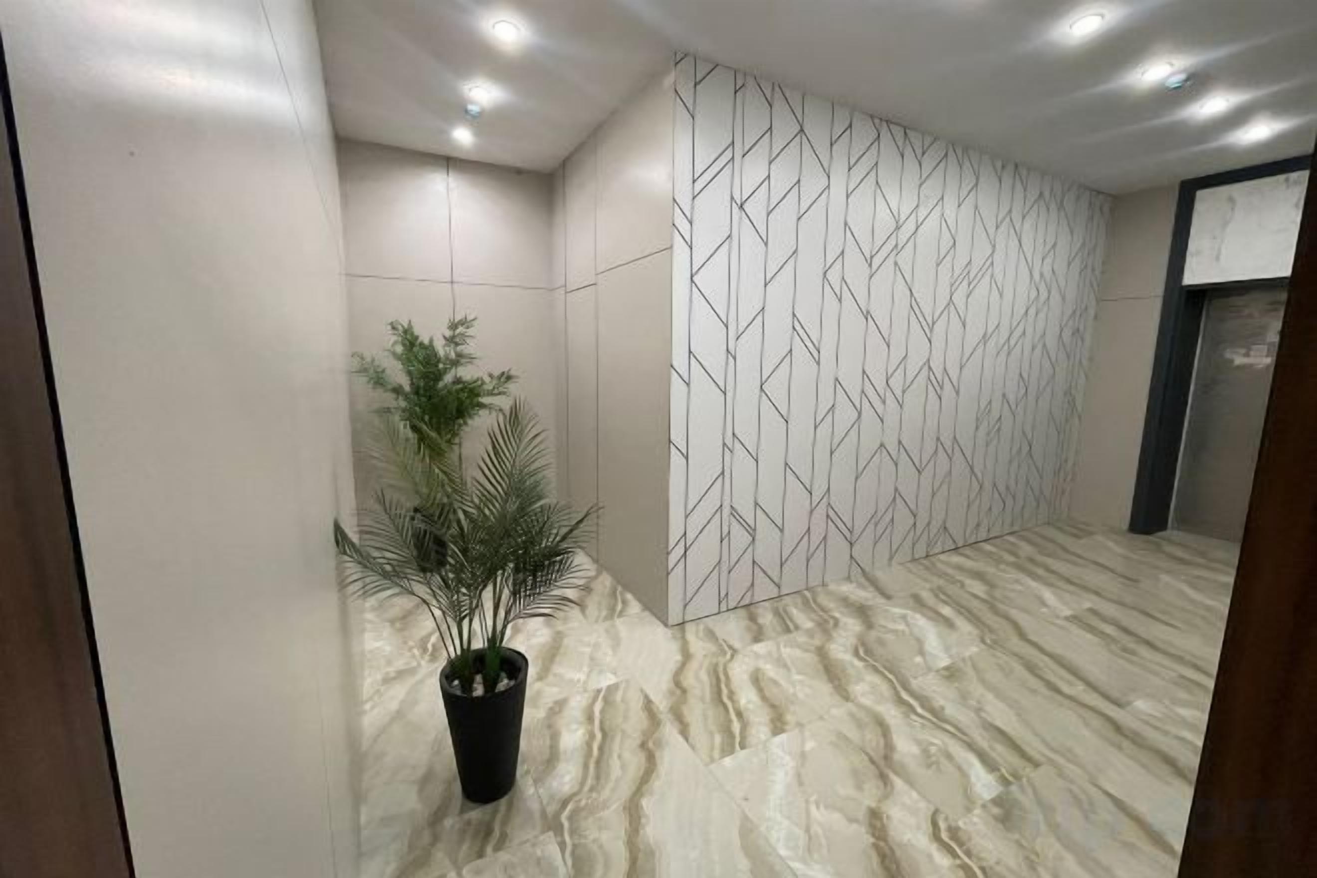 A hallway with a marble floor, a potted plant, and a wall with a geometric pattern.