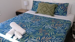 Una cama bien hecha con una colcha de hojas azules y verdes, una almohada de color verde y toallas blancas sobre la cama.