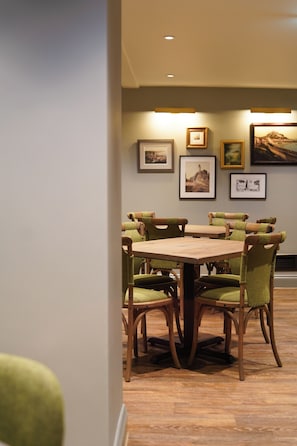 Un comedor con mesa y sillas de madera, cuadros en la pared y suelo de madera.