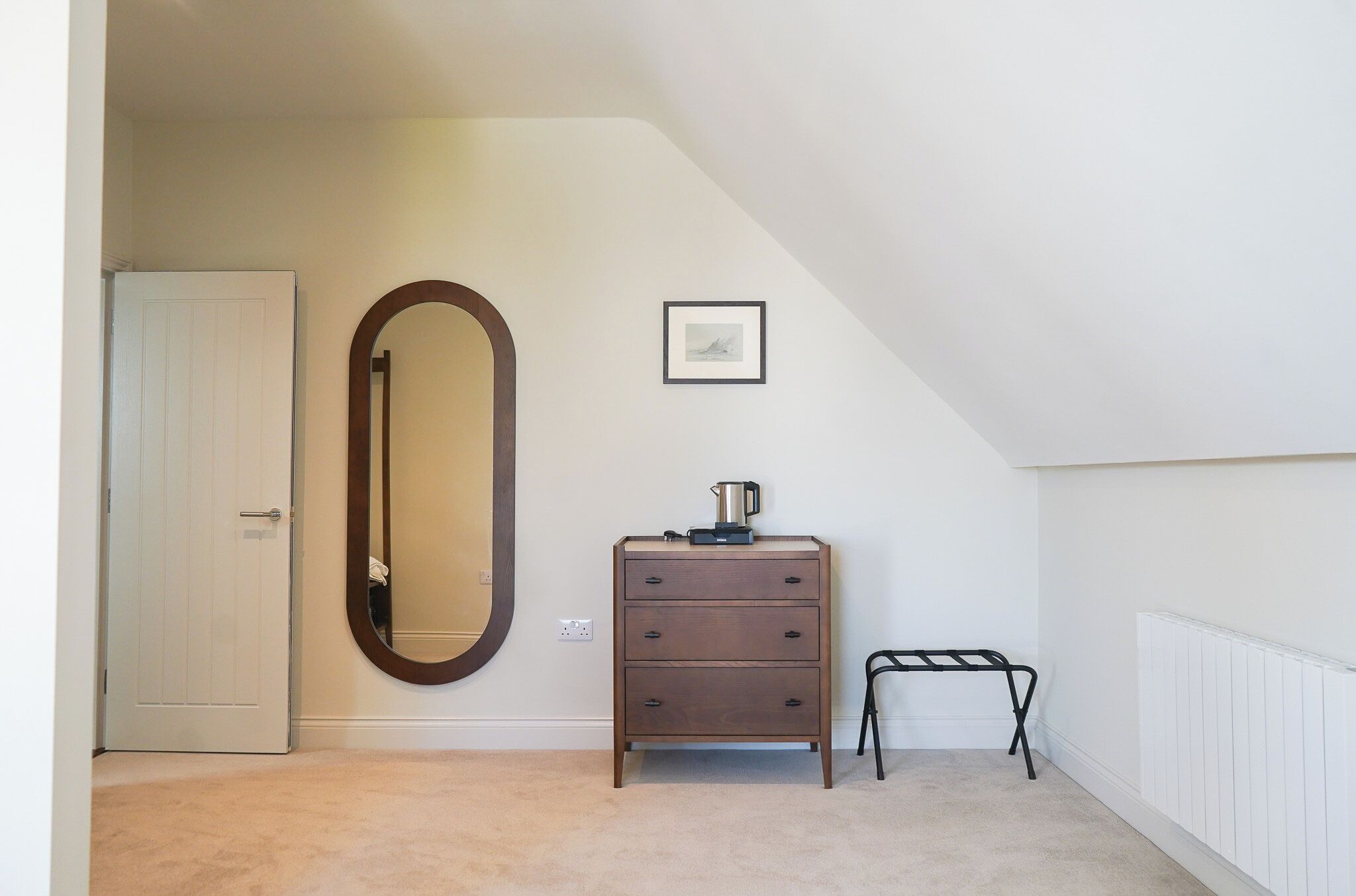 A bedroom with a dresser, a mirror, a radiator, and a framed picture on the wall.