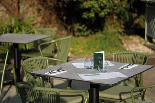 Un área de comedor al aire libre con sillas y mesas de metal verde, un menú y un vaso de agua sobre la mesa.