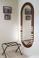Una habitación con un espejo ovalado grande con luces, un banco de metal negro y tres cuadros en la pared.