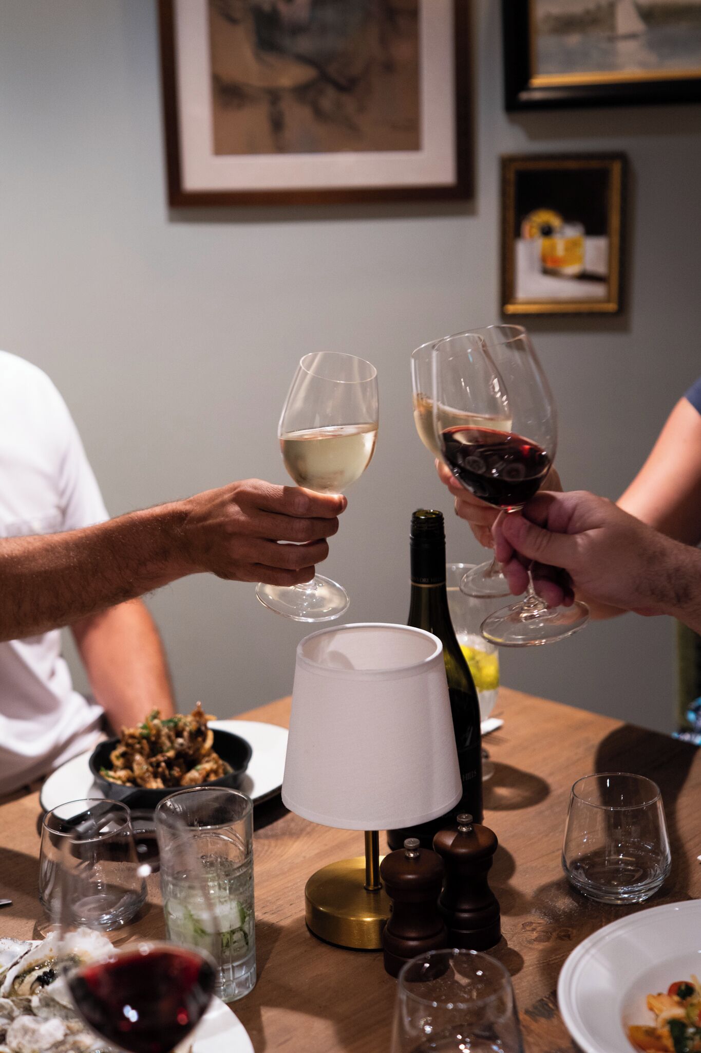 A dining table with wine glasses, a bottle, and a lamp.