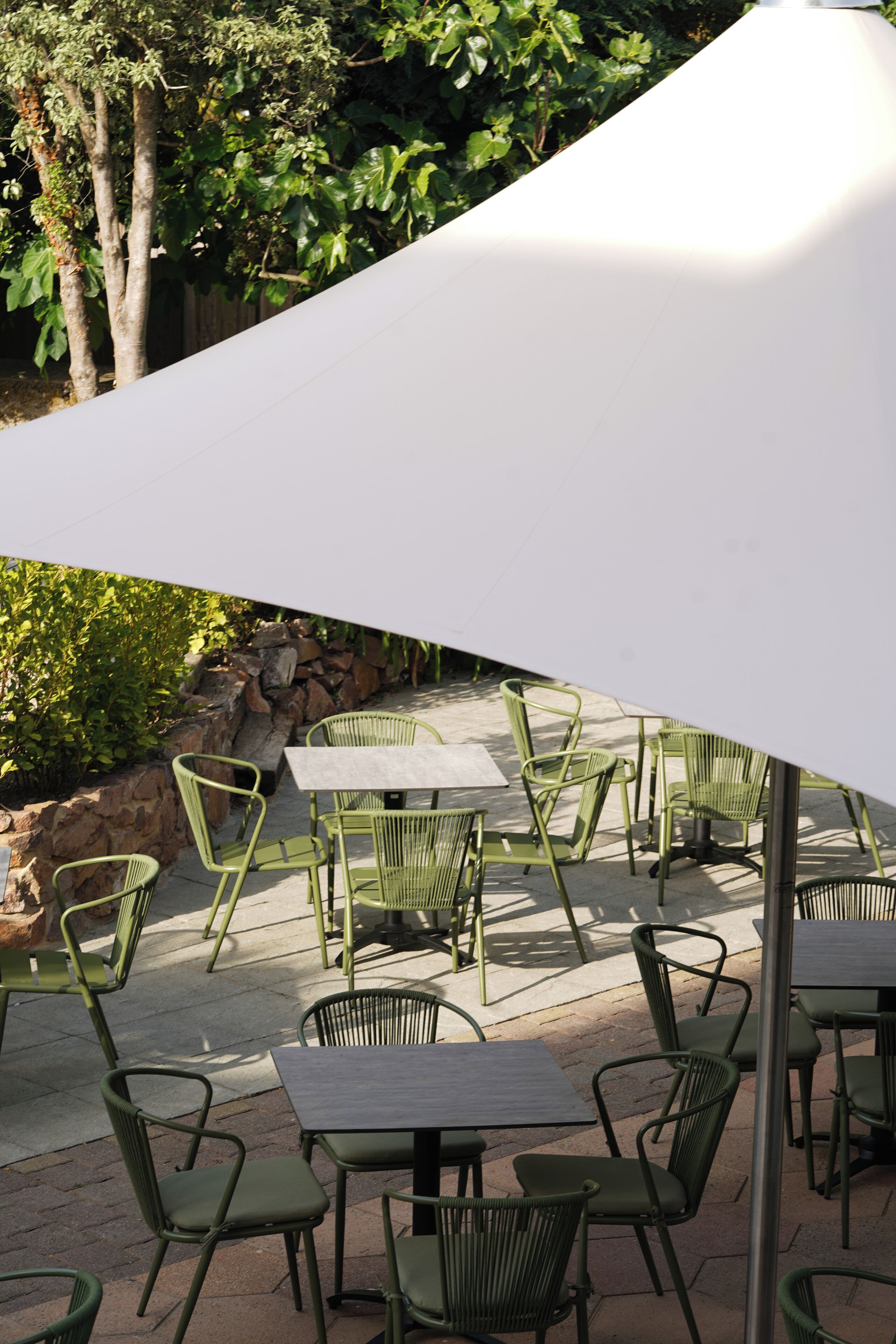 Outdoor patio seating with tables and chairs, surrounded by greenery and a stone wall.