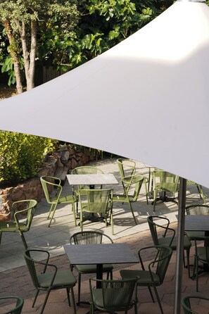 Outdoor patio seating with tables and chairs, surrounded by greenery and a stone wall.