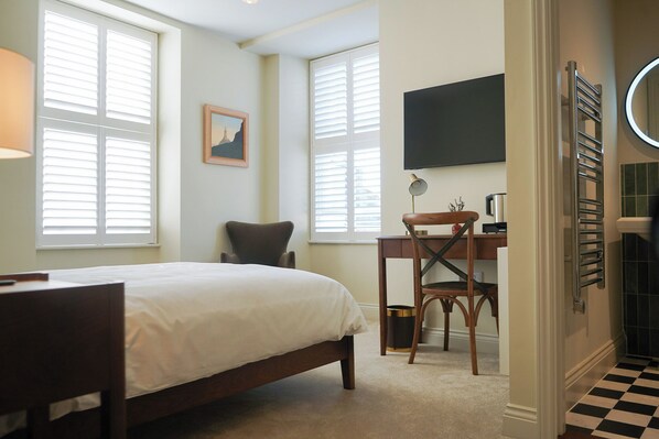A bedroom with a bed, a desk, a chair, a TV, and a radiator.
