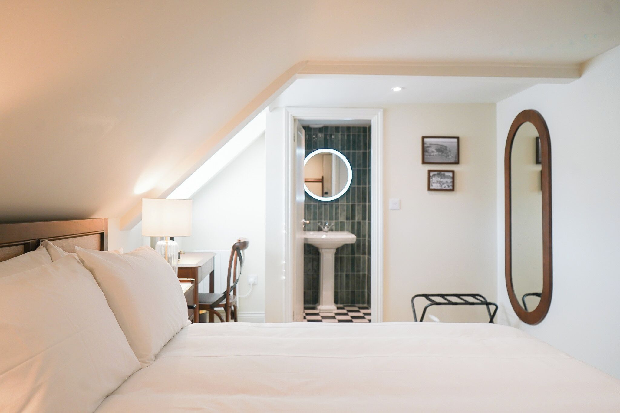 Ein Hotelzimmer mit einem Bett, einem Schreibtisch, einem Stuhl, einem runden Spiegel und einem Badezimmer mit Waschbecken und Fliesen.