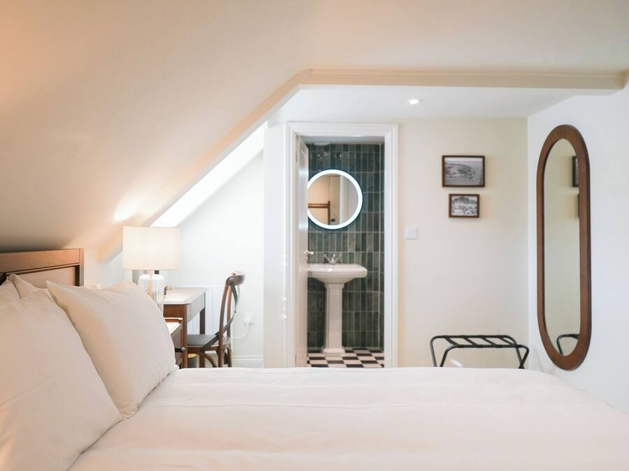 Ein Hotelzimmer mit einem Bett, einem Schreibtisch, einem Stuhl, einem runden Spiegel und einem Badezimmer mit Waschbecken und Fliesen.