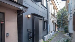A narrow alleyway between buildings with a black door, a security camera, and outdoor air conditioning units. - Shinjuku Haramachi Sugar&Spice (Tokyo)