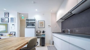 A modern kitchen with a wooden table, a chair, and a microwave. - Shinjuku Haramachi Sugar&Spice (Tokyo)