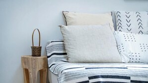 A bed with striped bedding, a wooden stool, and a woven basket. - Shinjuku Haramachi Sugar&Spice (Tokyo)