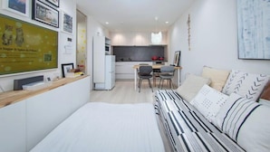 A modern, compact living space with a kitchenette, a dining area, and a bed with striped bedding. - Shinjuku Haramachi Sugar&Spice (Tokyo)