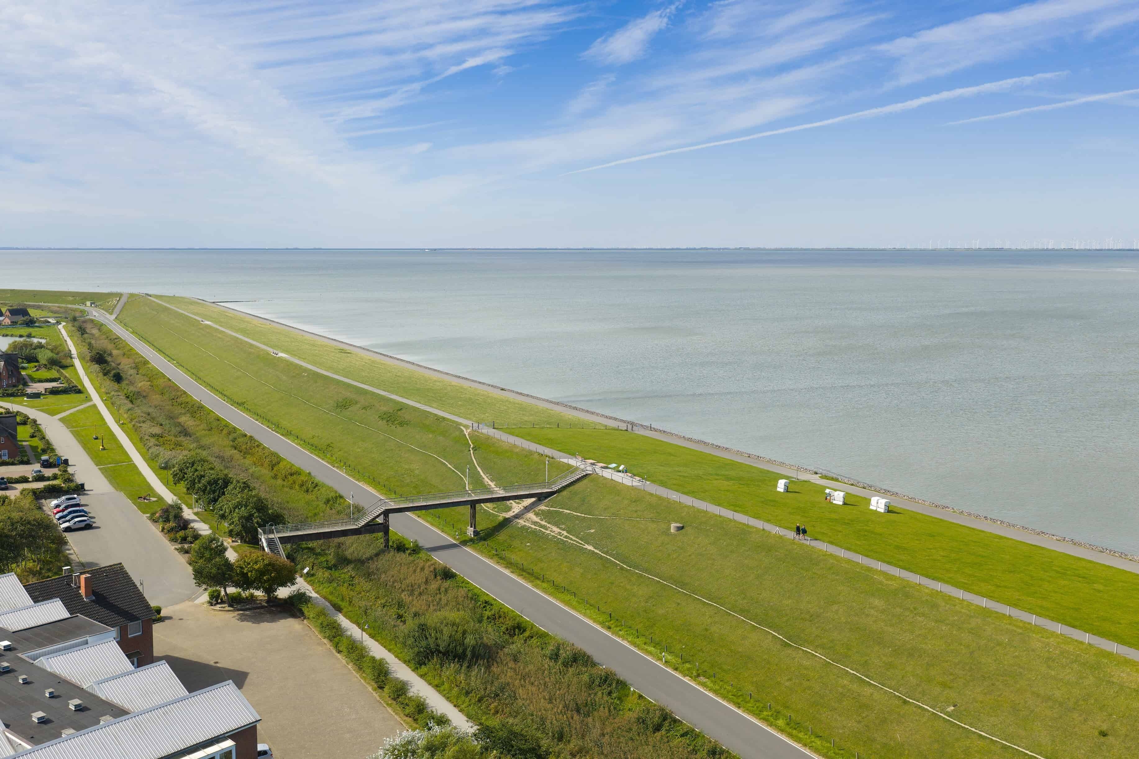 Luftaufnahme einer Küstenlandschaft mit einer Straße, Grünflächen und einem Gewässer.