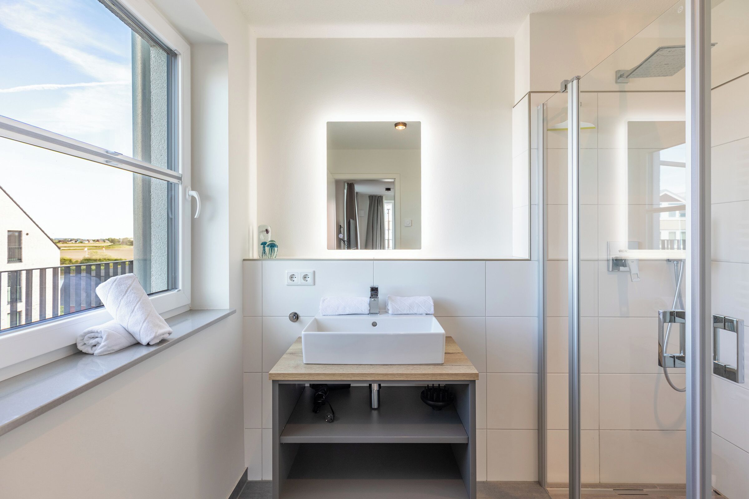 A modern bathroom with a large window, a sink, a mirror, and a shower.