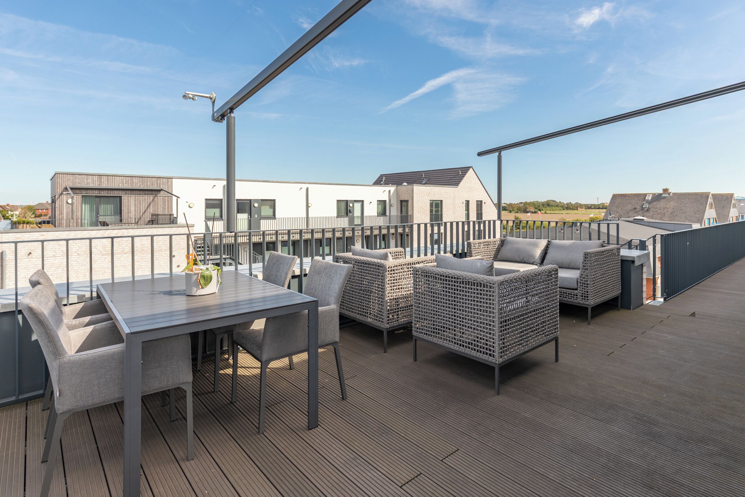 A rooftop terrace with a table and chairs, wicker furniture, and a view of surrounding buildings.