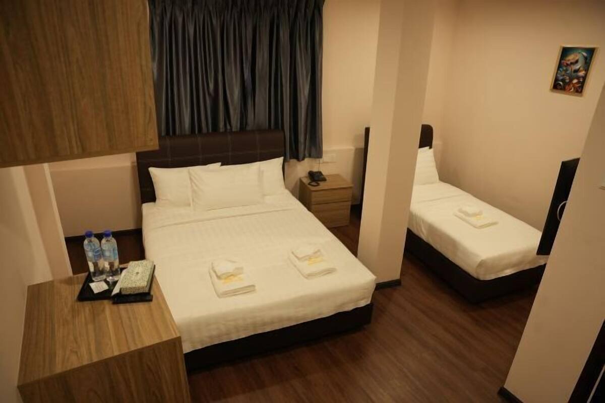 A hotel room with a bed, a smaller bed, a nightstand with a phone and water bottles, and a painting on the wall.